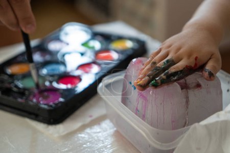 Foto de A child's hand paints an ice cube with colored paints, close-up photo - Imagen libre de derechos