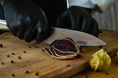 Photo for A chef in black gloves cuts basturma on a wooden board - Royalty Free Image