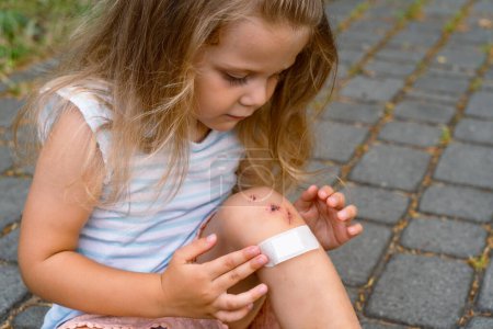 Ein kleines Mädchen legt nach einem Unfall ein Pflaster auf eine Wunde am Knie. Selektiver Fokus.