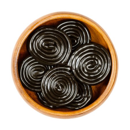 Photo for Liquorice wheels, in a wooden bowl. Licorice, is a confection, usually flavored and colored black with the extract of the roots of the liquorice plant Glycyrrhiza glabra, made with sugar and a binder. - Royalty Free Image
