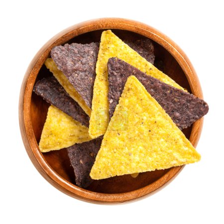 Photo for Yellow and blue tortilla chips, in a wooden bowl. Snack food, made from corn tortillas, cut into triangle shaped wedges, fried in oil and slightly salted. Close-up, from above, isolated, macro photo. - Royalty Free Image