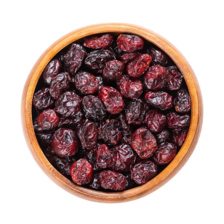 Dried large cranberries, in a wooden bowl. Ripe fruits of Vaccinium macrocarpon, also known as American cranberry or bearberry. Red berries with acidic taste. Isolated, from above, macro food photo.