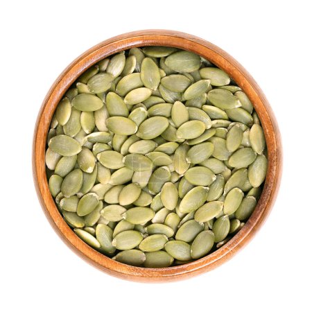 Photo for Pepitas, hulled pumpkin seeds, in a wooden bowl. Edible pumpkin seeds after shelling. Dried, raw seeds, flat and oval, with a light green color. Roasted and spiced, they are used as snack food. Photo. - Royalty Free Image