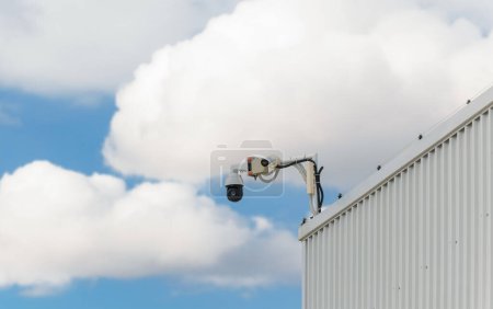 Téléchargez les photos : Caméra de surveillance CCD montée sur un hangar devant un ciel bleu nuageux. Technologie de caméra de sécurité numérique concept de surveillance pour la sécurité des biens. - en image libre de droit