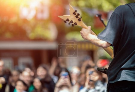 Back view of a male musician guitarist on stage with audience in a crowded concert. Heavy metal band performing on stage.