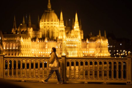 Photo for Budapest, Hungary People crossing the Margaret bridge with a view over the Illuminated Parliament building at night. - Royalty Free Image