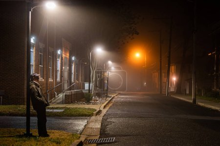 Téléchargez les photos : Solomons Island, Maryland, USA Un homme se tient contre un lampadaire par une nuit brumeuse. - en image libre de droit