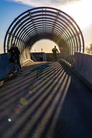 Photo for Copenhagen, Denmark A bicyclist and a jogger on a covered bridge over the railway track in the Amager district. - Royalty Free Image