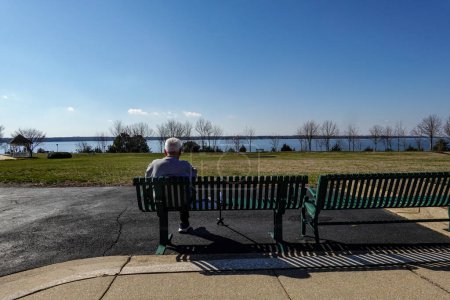 Foto de Solomons, Maryland EE.UU. Un hombre mayor se sienta en un banco al aire libre con vistas al río Patuxent durante el día. - Imagen libre de derechos