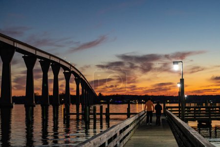 Solomons, Maryland USA A young couple on a pier below the the Solomons Bridge at night, or Gov. Thomas Johnson Bridge