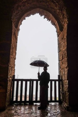 Photo for Ajlun, Castle, Jordan A tourist with umbrella visits the castle under an arch in the rain. - Royalty Free Image