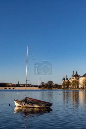 Photo for Copenhagen, Denmark An anchored saliboat with tarp on  the Peblinge Lake and residential buildings - Royalty Free Image