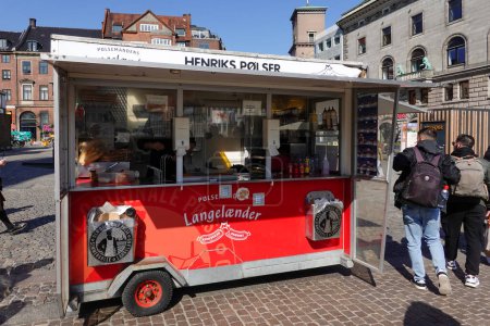 Foto de Copenhague, Dinamarca Un pequeño vagón rojo vende perritos calientes y salchichas danesas en una plaza del casco antiguo. - Imagen libre de derechos