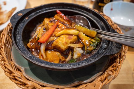 A typical Cantonese Chinese hot pot dish with Szechuan spices and tofu in an iron pot at a restaurant.
