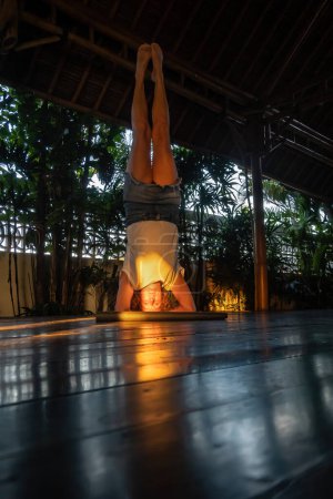 Téléchargez les photos : Ubud, Bali, Indonésie Une femme fait un appui-tête de yoga dans un shala de yoga au soleil couchant. - en image libre de droit
