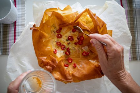 Téléchargez les photos : Une quiche de pâtisserie filo au fromage et une main appliquant des piments rouges - en image libre de droit