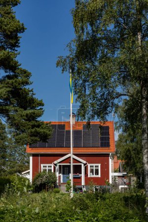 Téléchargez les photos : Nusnas, Suède 13 juillet 2023 Une maison résidentielle rouge alimentée par énergie solaire et un mât avec drapeau suédois. - en image libre de droit