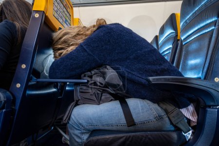 Photo for Stockholm, Sweden Sept 20, 2023 A woman leaning over on an airplane seat table to rest and sleep on a Ryanair flight within Europe. - Royalty Free Image