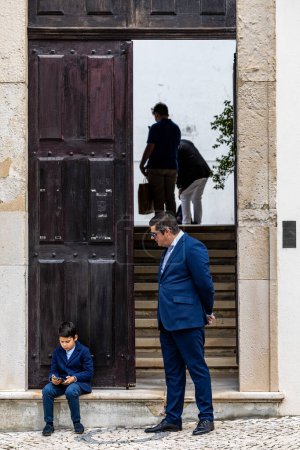 Photo for Aveiro, Portugal Sept 20, 2023 A young boy plays on his mobile phone at the  Igreja Da Misericordia De Aveiro, or Church Of Mercy as a grown up man looks on. - Royalty Free Image