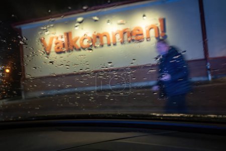 Foto de Varnamo, Suecia Dic 21, 2023 Un hombre pasa por el parabrisas de un coche estacionado y un cartel dice Welcome in Swedish. - Imagen libre de derechos
