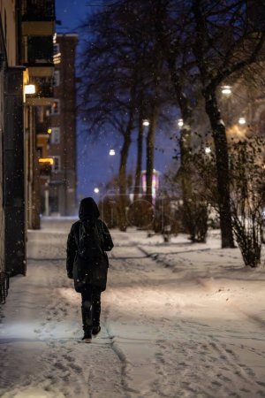 Téléchargez les photos : Stockholm, Suède Jan 2, 2024 Une femme marche seule en silhouette sur un trottoir enneigé dans le quartier Kungsholmen. - en image libre de droit