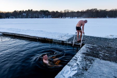 Téléchargez les photos : Stockholm, Suède Deux hommes se baignent sur la glace d'un quai dans un lac gelé. - en image libre de droit