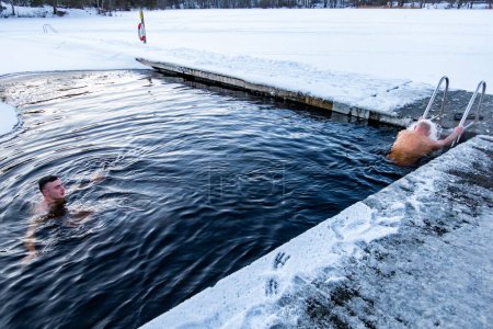 Téléchargez les photos : Stockholm, Suède Deux hommes se baignent sur la glace d'un quai dans un lac gelé. - en image libre de droit