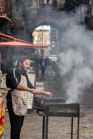 Foto de Palermo, Sicilia, Italia Jan 12, 2024 Un cocinero se para junto a una parrilla para fumar en el mercado de alimentos callejeros Mercato di Ballaro - Imagen libre de derechos