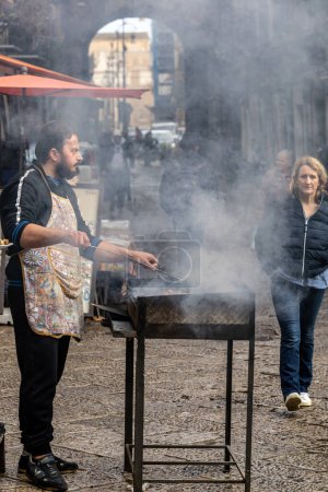 Foto de Palermo, Sicilia, Italia Jan 12, 2024 Un cocinero se para junto a una parrilla para fumar en el mercado de alimentos callejeros Mercato di Ballaro - Imagen libre de derechos