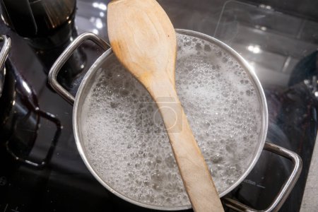 Hot pasta water boiling on a stove with a wooden spoon to prevent boil over.