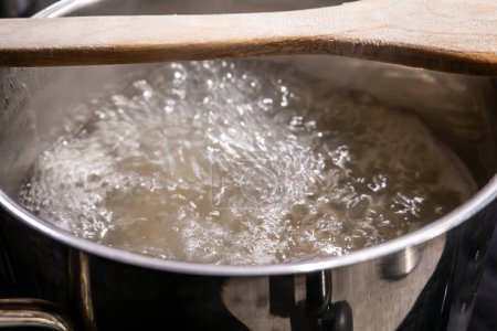 Hot pasta water boiling on a stove with a wooden spoon to prevent boil over.
