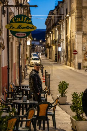 Téléchargez les photos : Pacentro, Italie 13 févr. 2024 Un homme se tient la nuit devant un café local sur la place. - en image libre de droit