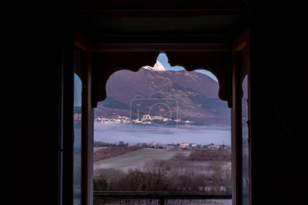 Castel di Ieri, Italie Vue panoramique sur les montagnes du Monte Sirente et le parc national des Abruzzes depuis une fenêtre ouverte dans un chalet au crépuscule.