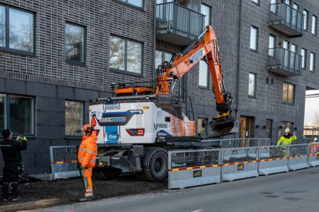 Photo for Stockholm, Sweden March 4, 2024 Elsa, Sweden's first all electric wheeled excavator, at work on a new housing construction project in the Sodermalm district. - Royalty Free Image