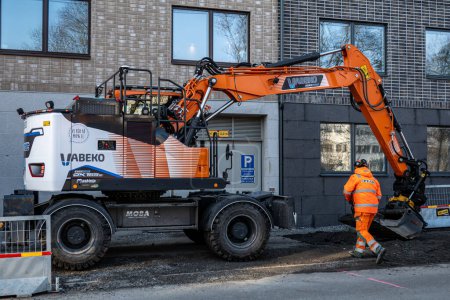 Photo for Stockholm, Sweden March 4, 2024 Elsa, Sweden's first all electric wheeled excavator, at work on a new housing construction project in the Sodermalm district. - Royalty Free Image