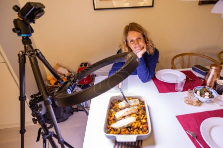 Foto de Una mujer en una mesa de cena comprueba si el salmón está bien cocinado bajo una cámara y equipo de iluminación. - Imagen libre de derechos