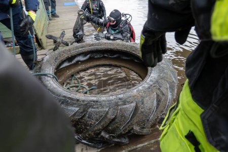 Téléchargez les photos : Stockhom, Suède 1 avril 2024 Un plongeur et des bénévoles ramassent des ordures comme un gros pneu de tracteur au fond du canal Palsundet au centre-ville de Stockholm. - en image libre de droit