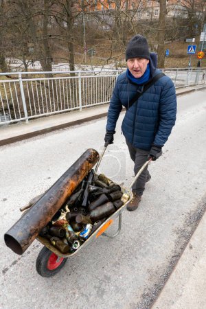 Téléchargez les photos : Stockhom, Suède Un homme pousse une brouette avec des bouteilles en verre ramassées dans l'eau par des plongeurs dans le canal Palsundet au centre-ville de Stockholm. - en image libre de droit