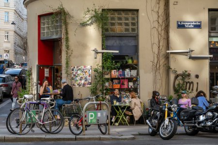 Foto de Viena, Austria 5 de abril de 2024 Personas en un café al aire libre rodeado de motocicletas y bicicletas Gumpendorfer Strasse. - Imagen libre de derechos