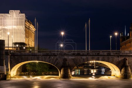 Foto de Estocolmo, Suecia El agua dulce del lago Malaren corre bajo el puente Norrbro en el cuerpo de agua Norrstrom en el centro de la ciudad por la noche en el Mar Báltico. - Imagen libre de derechos
