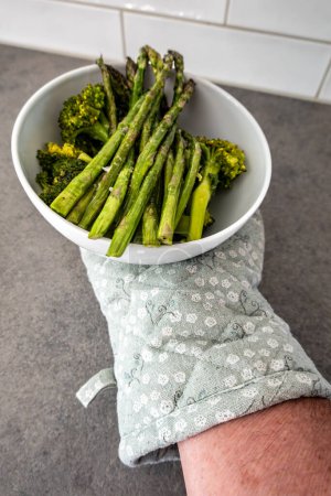 A hand holds cooked asparagus in a bowl with broccoli.