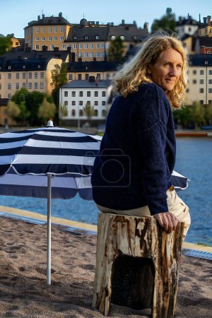 Estocolmo, Suecia Junio 17, 2024 Una mujer se sienta en una playa de arena artificial en Gama Stan o en el casco antiguo en el sol de la noche de verano en Riddarfjarden.