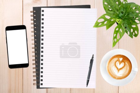 Foto de Un cuaderno en blanco abierto, un smartphone con bolígrafo y una taza de café con leche sobre una mesa de madera - Imagen libre de derechos