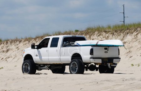 Foto de Savage Ditch, Delaware, Estados Unidos - 4 de julio de 2023 - Un camión Ford blanco con un permiso de pesca de kayak y surf en la playa conduciendo en la arena - Imagen libre de derechos