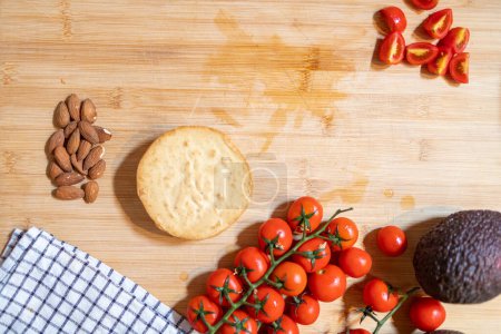 Foto de Vista superior del queso de almendras vegano en la tabla de madera con almendras crudas al lado y tomate cherry - Imagen libre de derechos
