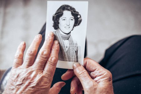 Foto de CIRCA 1970: Las manos de una anciana sosteniendo una foto en blanco y negro de la joven. Concepto del paso del tiempo - Imagen libre de derechos