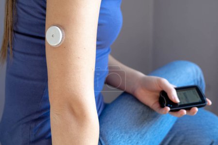 Photo for Girl sitting with flash glucose monitor, patch on her hand holding monitor - Royalty Free Image