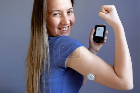 Foto de Chica mostrando su monitor de glucosa flash con nivel normal de azúcar en sangre, parche en la mano - Imagen libre de derechos