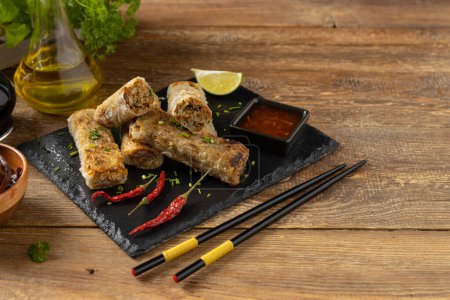 Portion of spring rolls stuffed with meat. Served with sauce. Natural wood background.