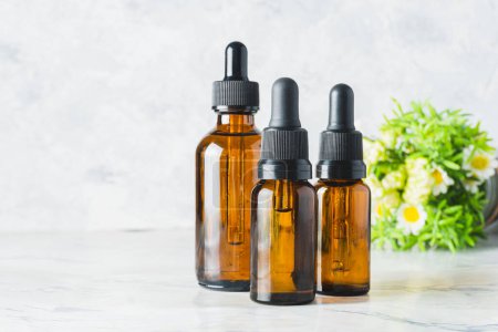 Photo for Three essential oil dropper bottles with chamomile flowers out of focus in the background. background with copy space - Royalty Free Image